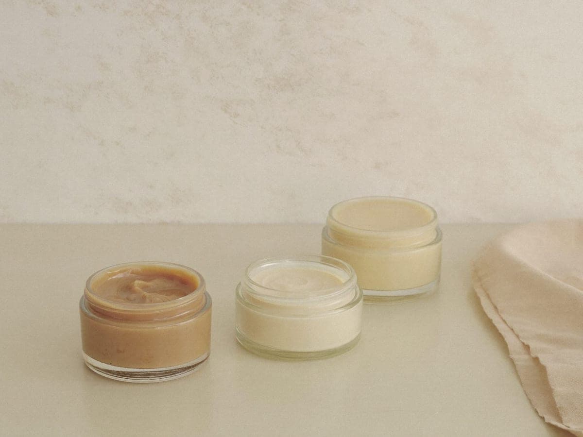 Three open jars of body butter on a pale surface