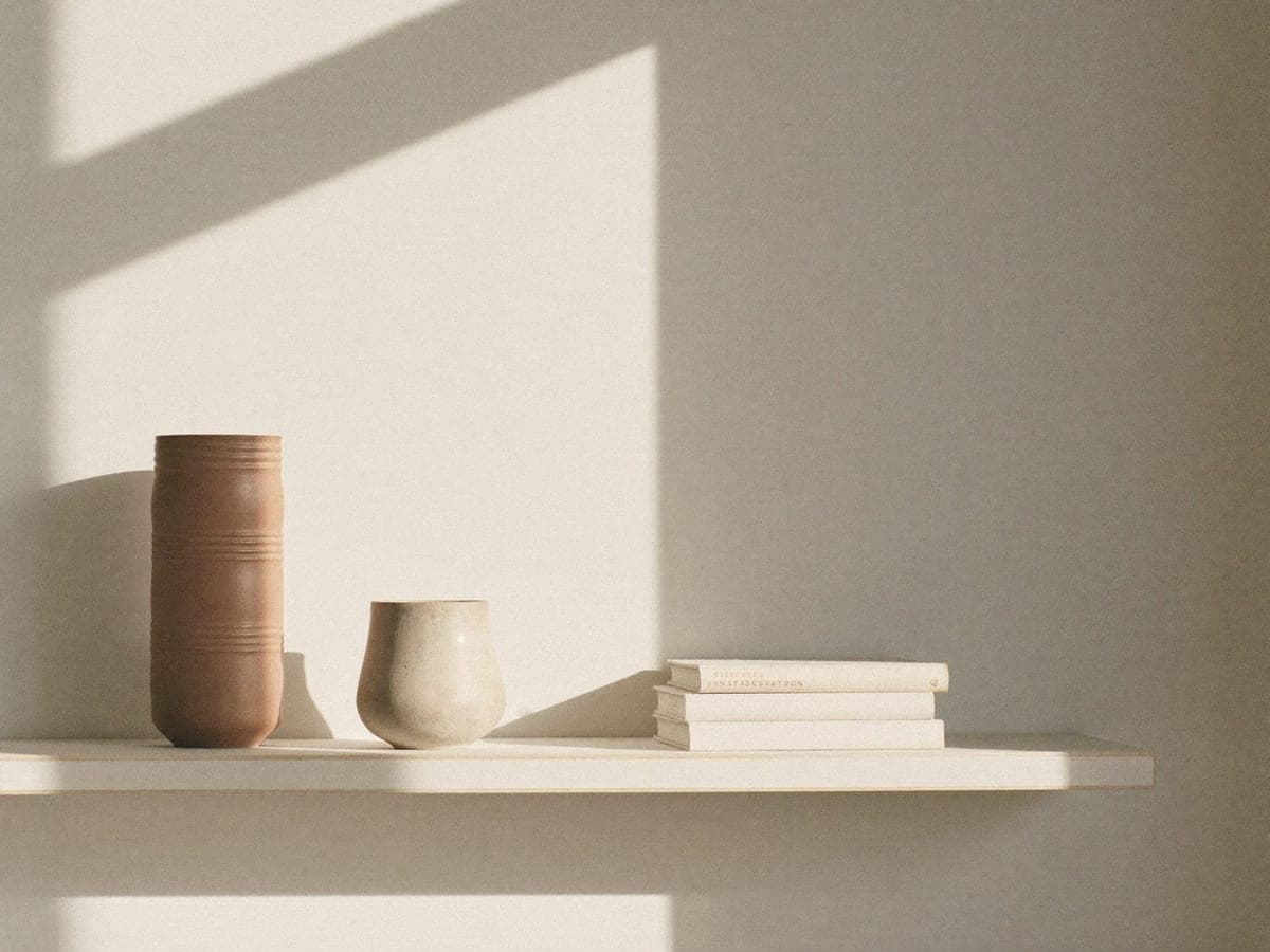 A shelf with a terracotta vessel, a ceramic cup and books in raking light