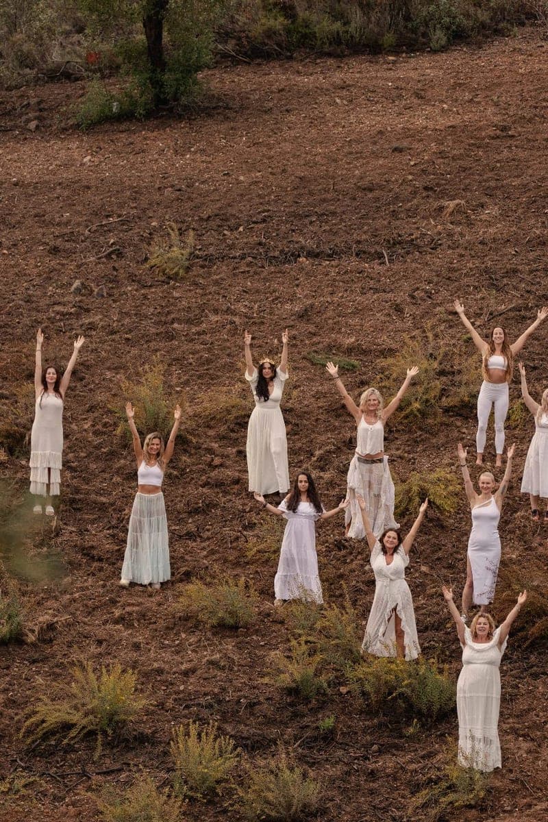 Women in white standing apart across an open field, arms raised