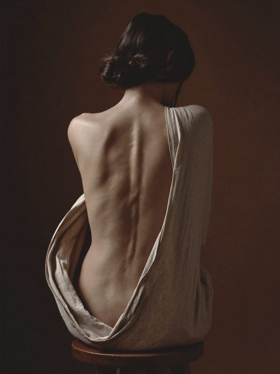 A seated figure seen from behind, the line of the spine catching the light