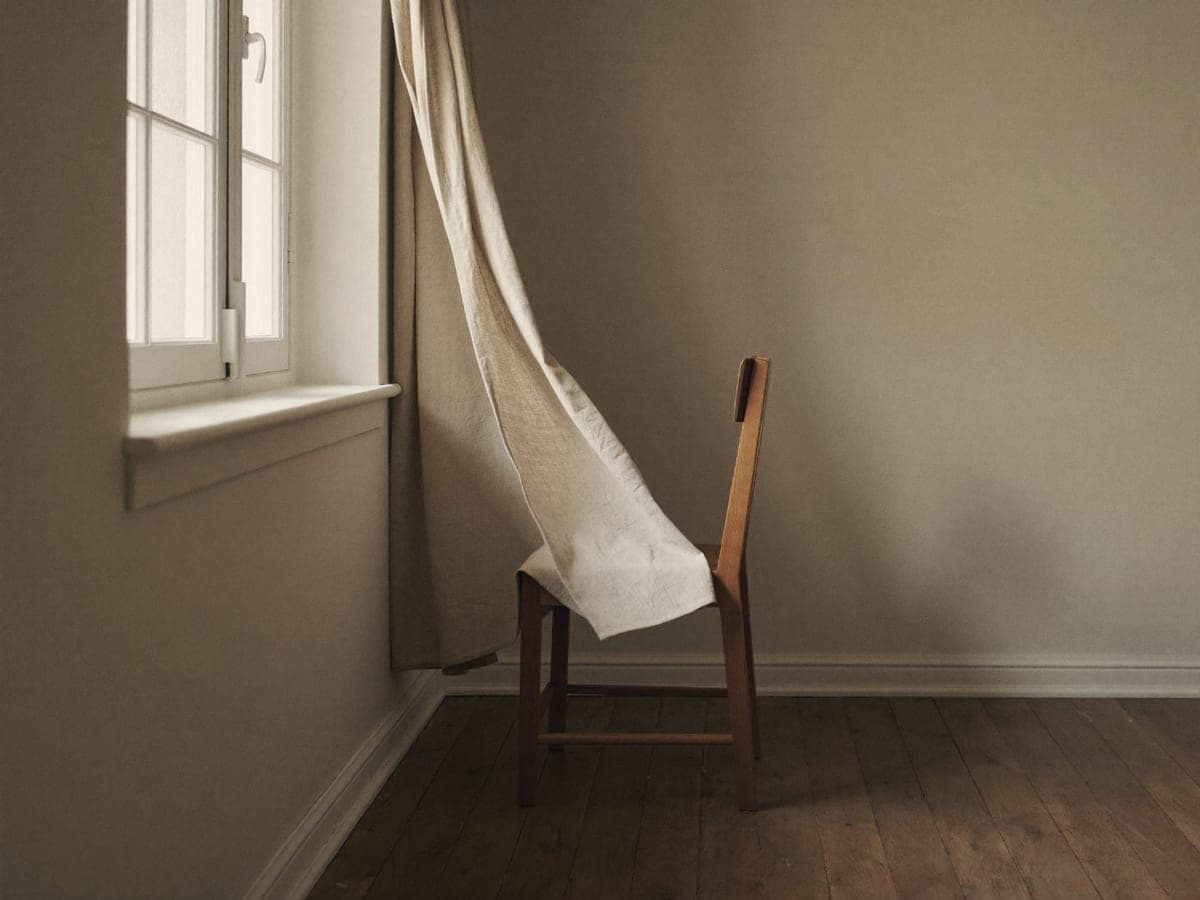 An empty chair by a window, a linen sheet draped over its back
