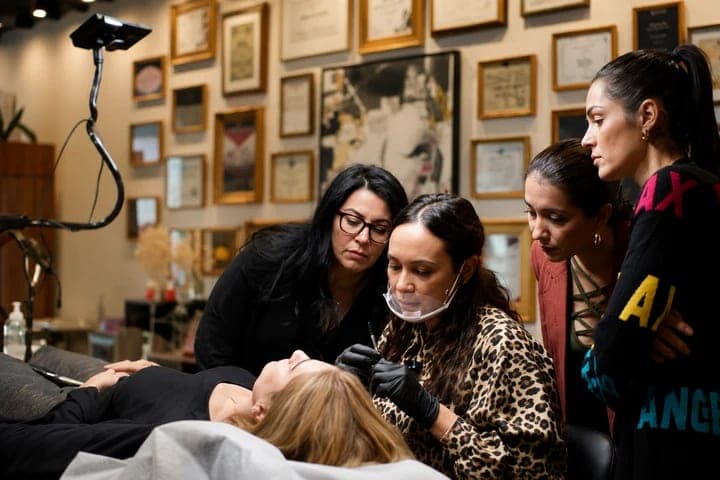 Camila working on a client while three artists watch closely during a training session