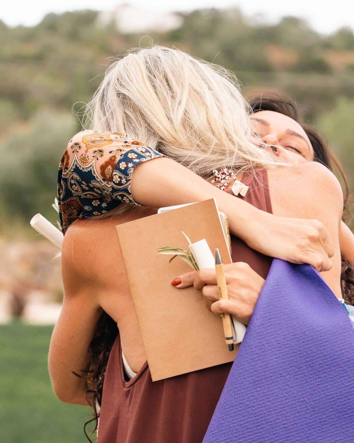 Two women embracing outdoors, one still holding her journal and pen