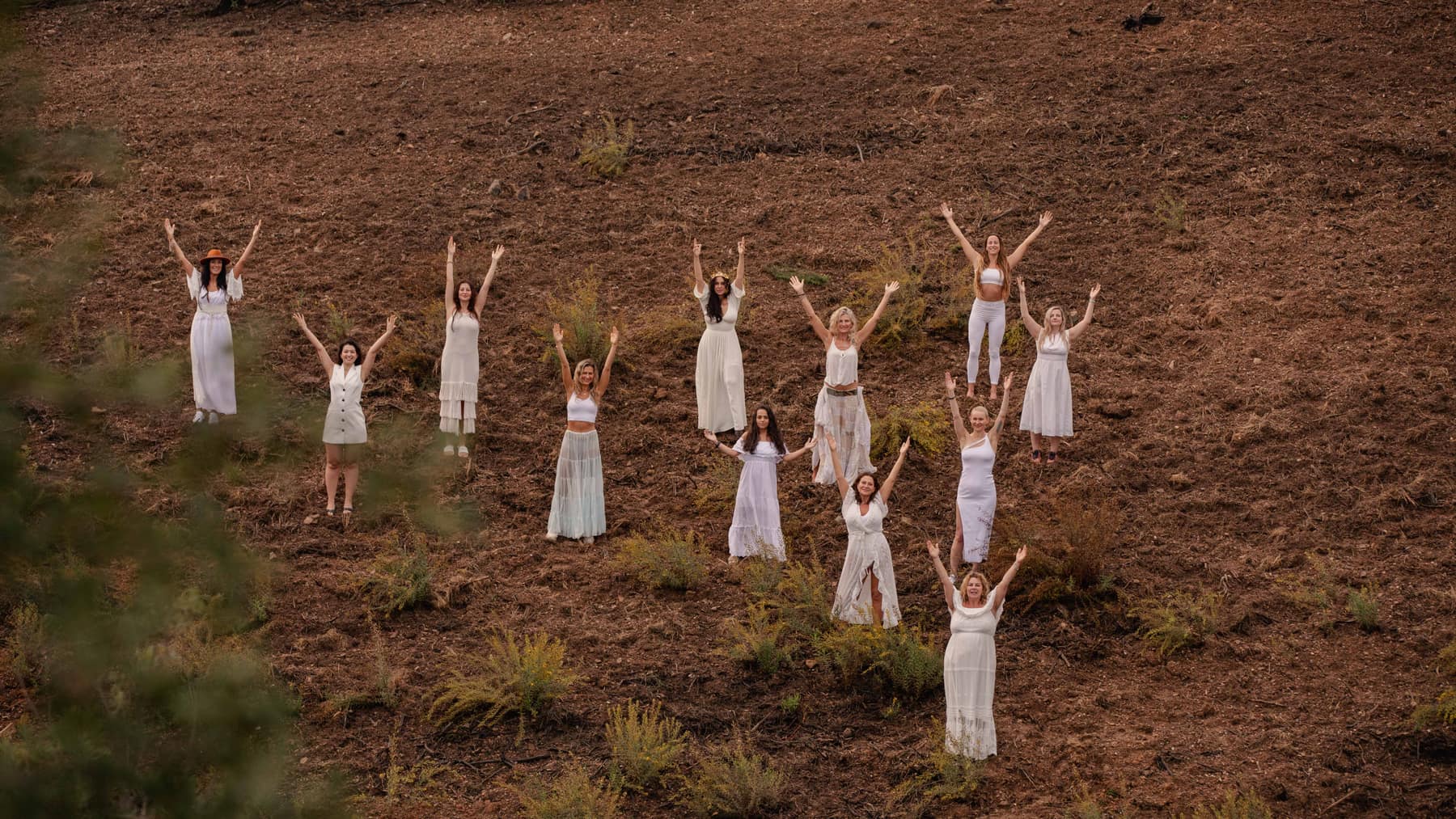 Women in white standing apart across an open field, arms raised