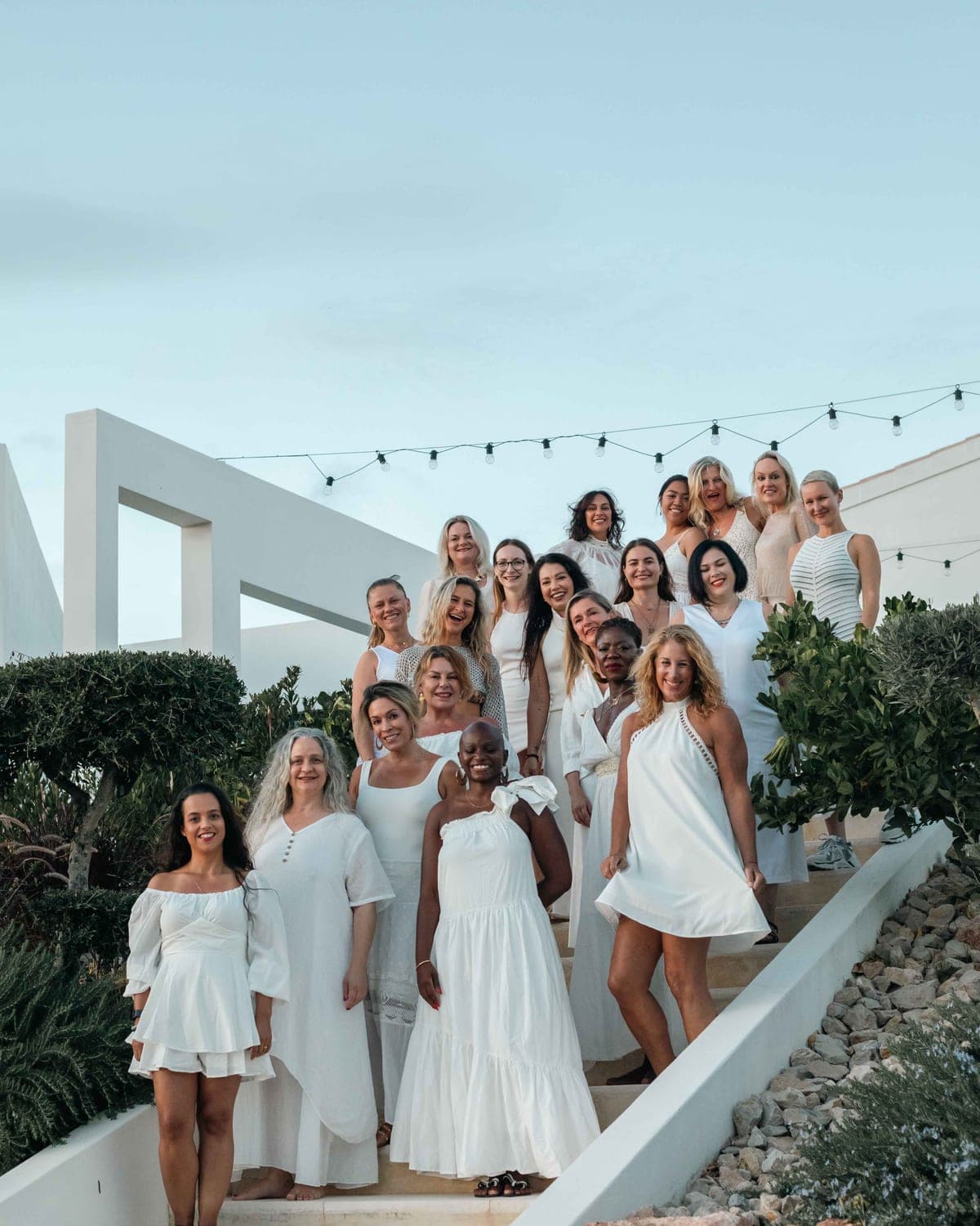 Around twenty women dressed in white, gathered on stone steps at dusk